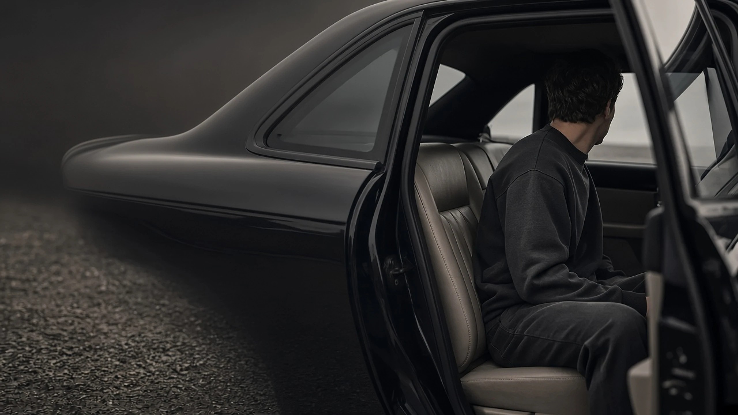 Model in a charcoal midweight crewneck sweatshirt seated in the rear of a dark leather sedan.